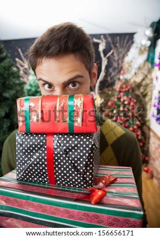 Portrait of young man with raised eyebrows looking over stacked Christmas gifts in store