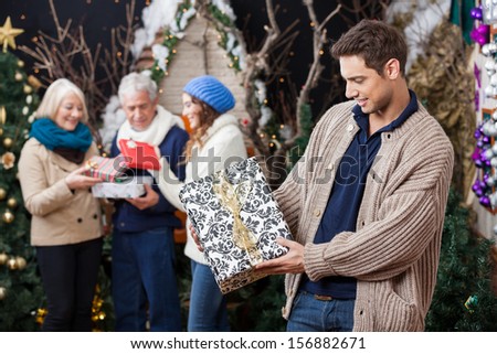 Young man looking at Christmas present with family standing in background at store