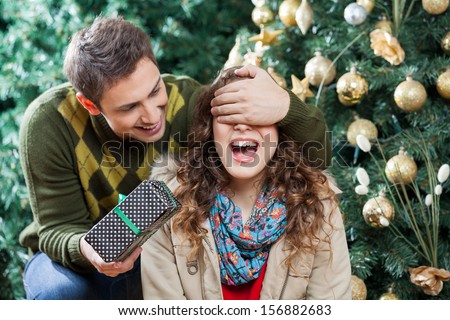 Young Man Covering Woman\'S Eyes While Surprising Her With Gift In Christmas Store