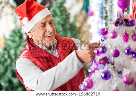 Happy male owner in Santa hat decorating Christmas tree at store