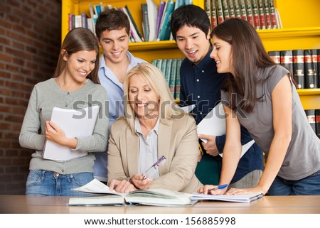 Happy university teacher with book explaining students in library