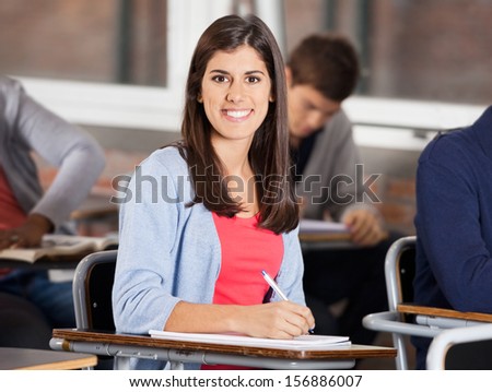 Portrait of confident female student sitting at desk in classroom