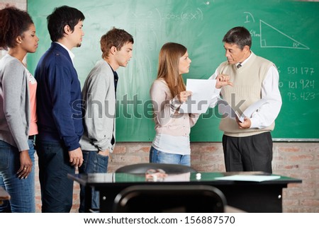 Mature teacher gesturing thumbsdown while looking at female student in classroom