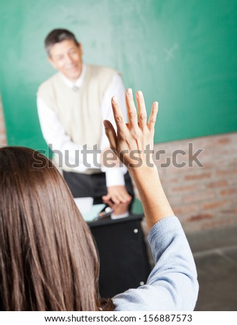 Rear view of young college student raising hand to answer in classroom