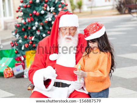 Girl showing wish list to Santa Claus in courtyard