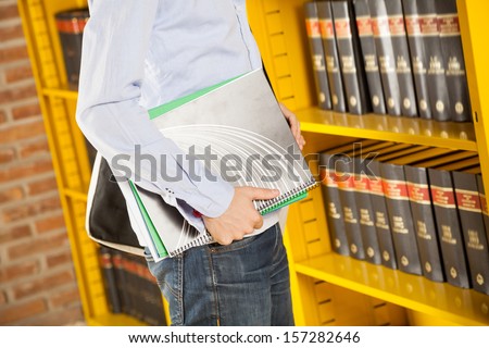 Midsection of young student holding books in college library