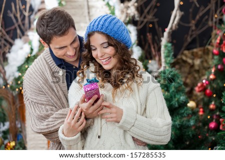 Happy young couple with Christmas present standing at store