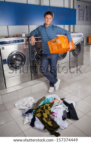 Portrait of happy young man holding empty basket with dirty clothes on floor at laundry