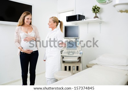 Female gynecologist showing bed to pregnant woman in examination room