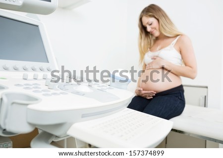 Pregnant woman holding tummy sitting by ultrasound machine in clinic