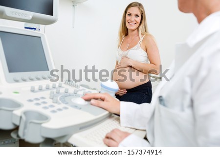 Happy pregnant woman looking at obstetrician using ultrasound machine in clinic