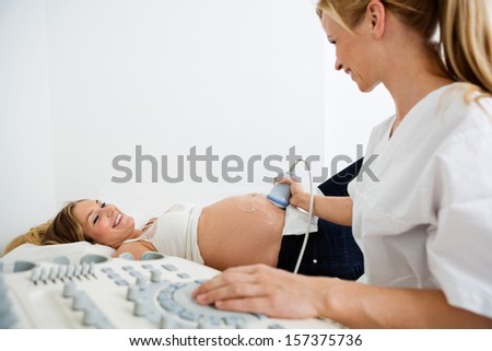 Ultrasound technician scanning pregnant woman\'s belly in clinic