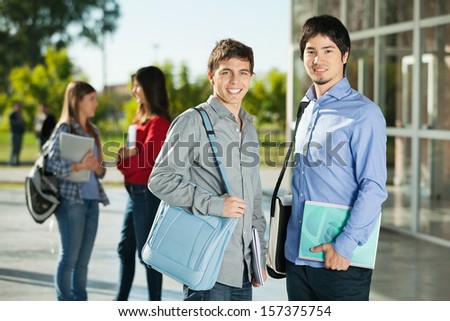 Portrait of happy male students with friends standing in background on college campus