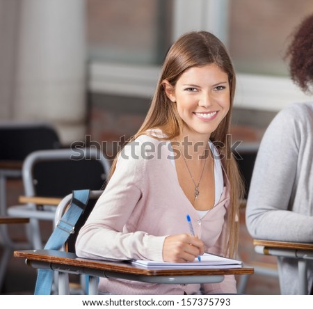Portrait of beautiful university student sitting at desk with friend in classroom
