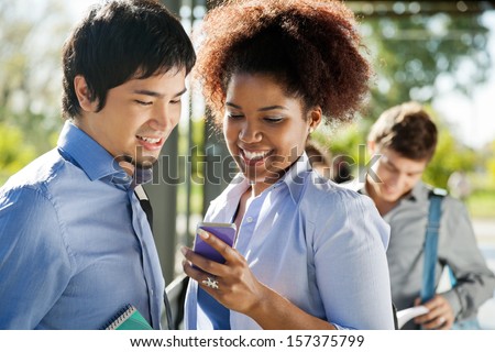 Happy young friends reading text message on cellphone in college campus