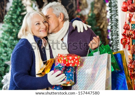 Senior man with shopping bags kissing woman at Christmas store