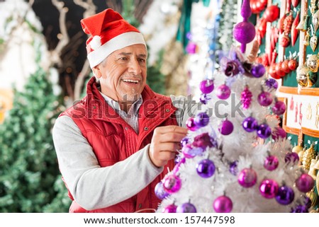 Happy male owner decorating Christmas tree with balls at store