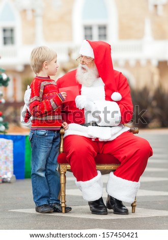 Full length of boy giving wish list to Santa Claus in courtyard
