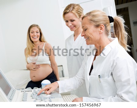 Happy female technicians using ultrasound machine with pregnant woman in clinic