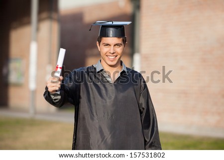 Portrait of confident male student showing diploma on graduation day at university campus