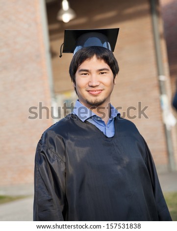 Portrait of confident male student in graduation gown and mortar board on college campus