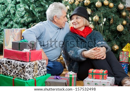 Senior couple looking at each other while sitting with presents on floor in Christmas store