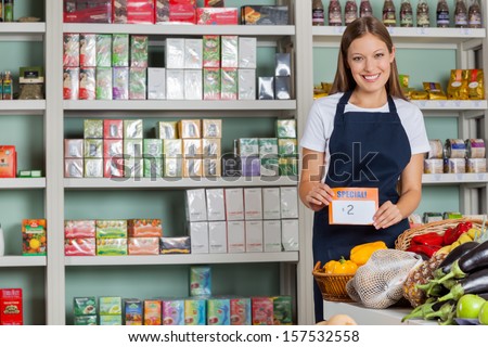 Portrait Of Confident Saleswoman Displaying Pricetag In Grocery Store
