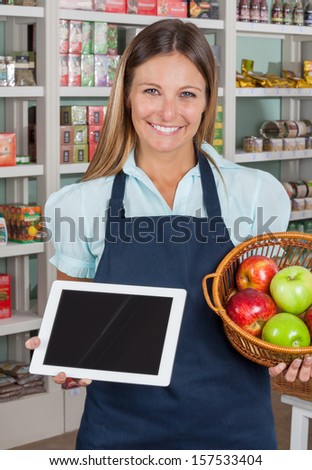Portrait of happy saleswoman holding digital tablet and fruits basket in grocery store