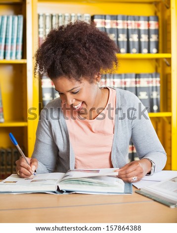Happy female student writing in book at university library