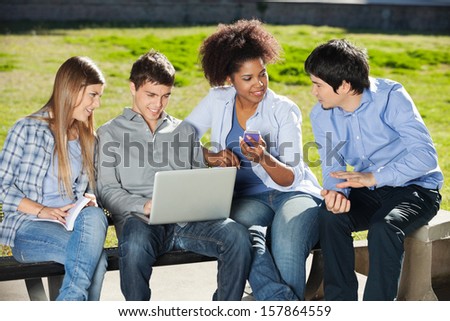 Young university students with laptop and mobilephone sitting in campus