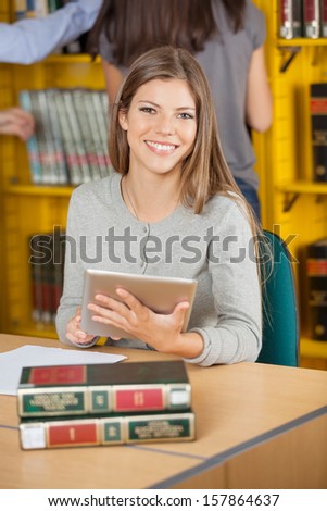 Portrait of happy female student with digital tablet studying in college library