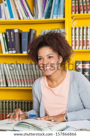 Beautiful college student with books and pen looking away in library