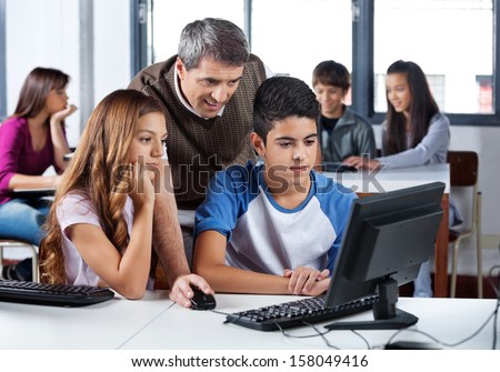 Mature male teacher assisting teenage school students in computer class