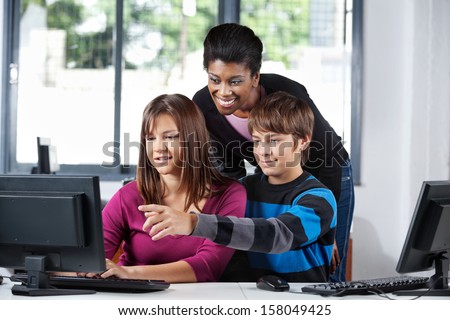 Young African American female teacher assisting teenage school students in computer lab