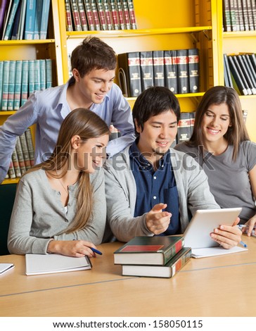 Happy multiethnic students with digital tablet discussing in college library