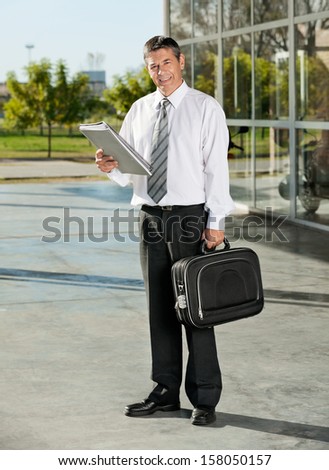 Full length portrait of college professor with books and bag at campus