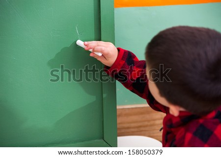 Little boy writing on green chalkboard in preschool