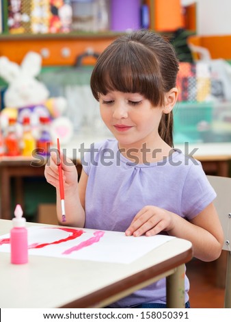 Cute little preschool girl painting at desk in art class