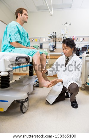 Full length of doctor examining male patient\'s reflexes with hammer
