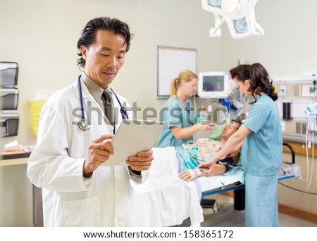 Male doctor examining report on digital tablet while nurses treating patient in hospital