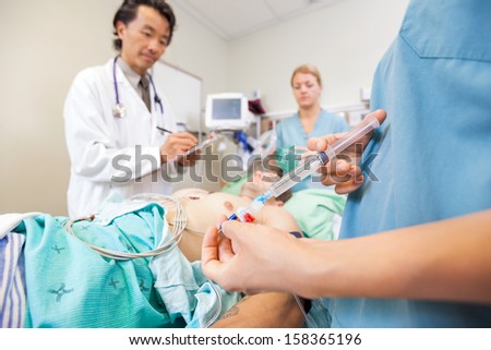 Midsection of nurse injecting dosage in IV tube while doctor and colleague examin patient at hospital