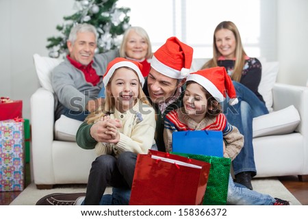 Happy children and father with gifts while family in background during Christmas at home