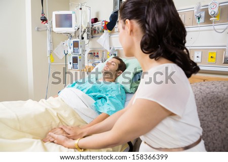 Young woman holding man\'s hand lying on bed in hospital