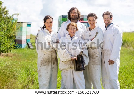 Team of confident male and female beekeepers standing together at apiary