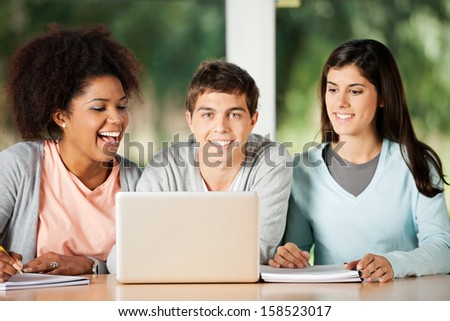 Portrait of happy male student with friends looking at laptop in classroom