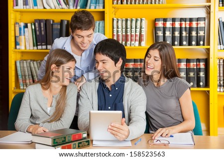 Group of happy college friends with digital tablet studying in library