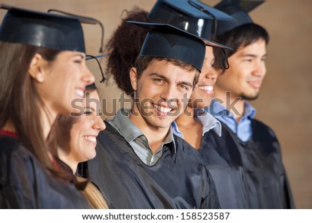 Portrait of happy young man standing with students on graduation day in college