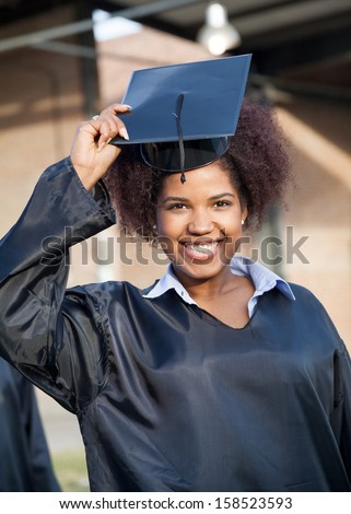 Portrait of happy female student in graduation gown wearing mortar board on university campus