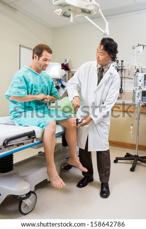 Full length of male neurologist examining patient\'s knee with hammer in hospital room