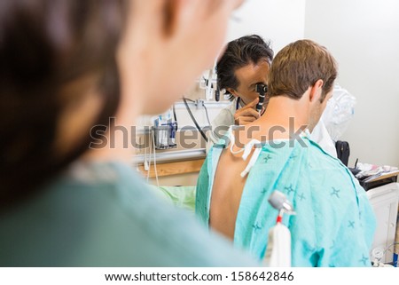 Male doctor using otoscope to examine patient\'s ear in hospital